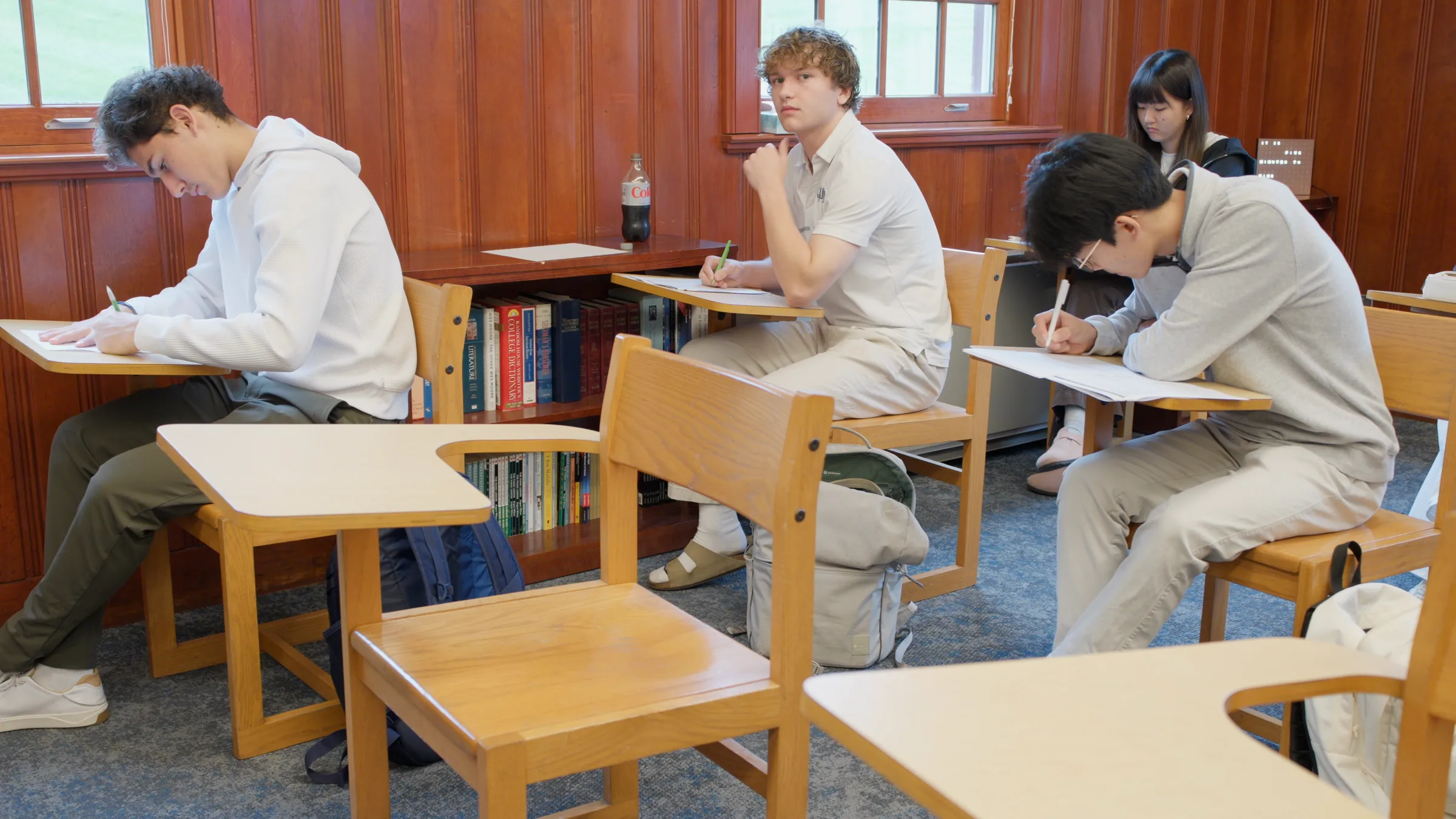 Alumnos escribiendo en sus pupitres durante una clase en un salón con paredes de madera en Canterbury School